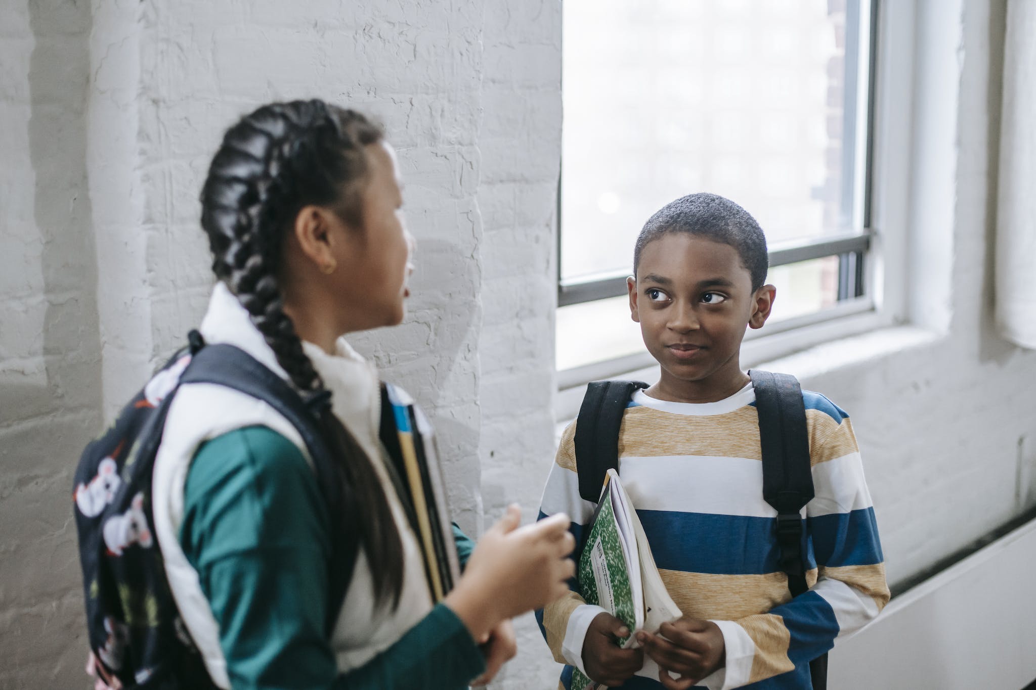 Content multiracial pupils with copybooks and backpacks standing in school corridor and having conversation